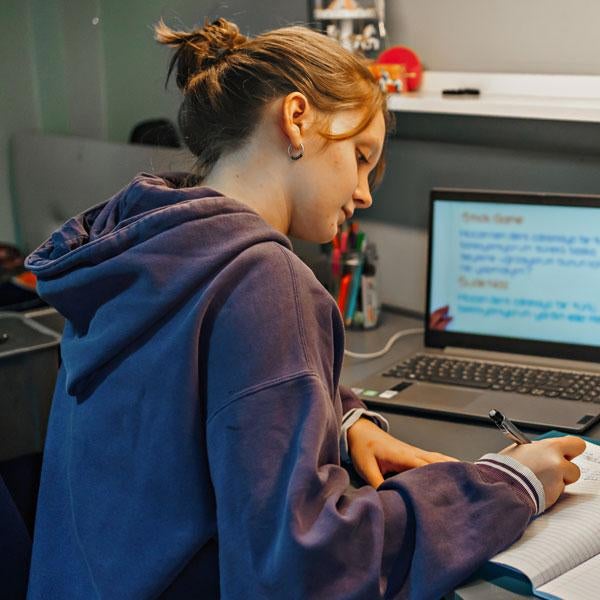 Student writing in notebook in front of computer